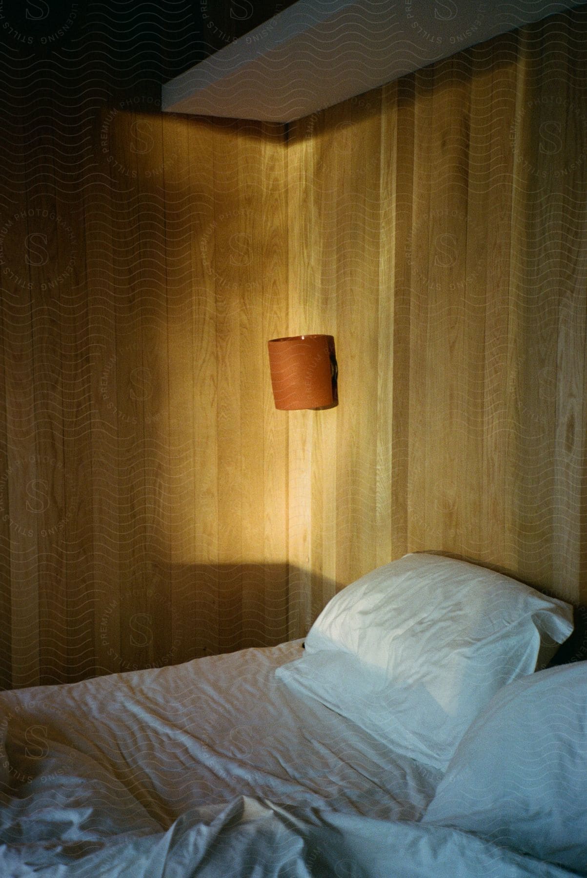 Orange lamp shade hanging from wooden wall in a bedroom