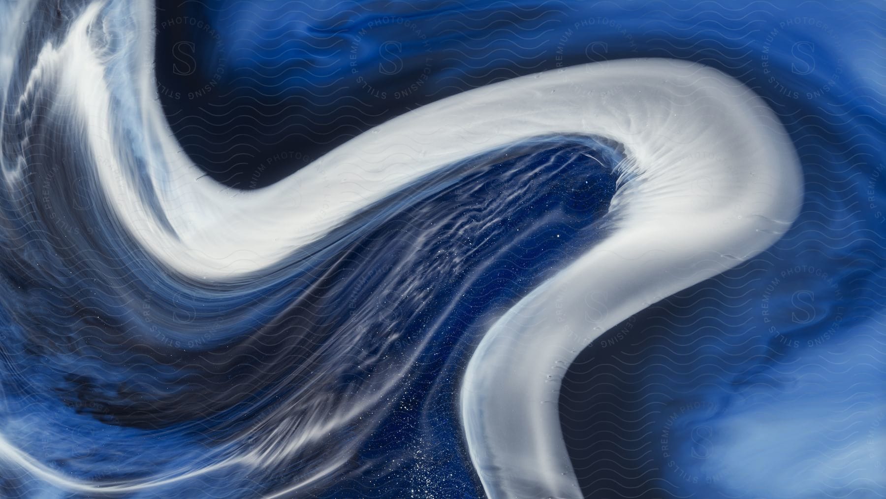 A white ribbon curves in a sideways sshape in blue fluid