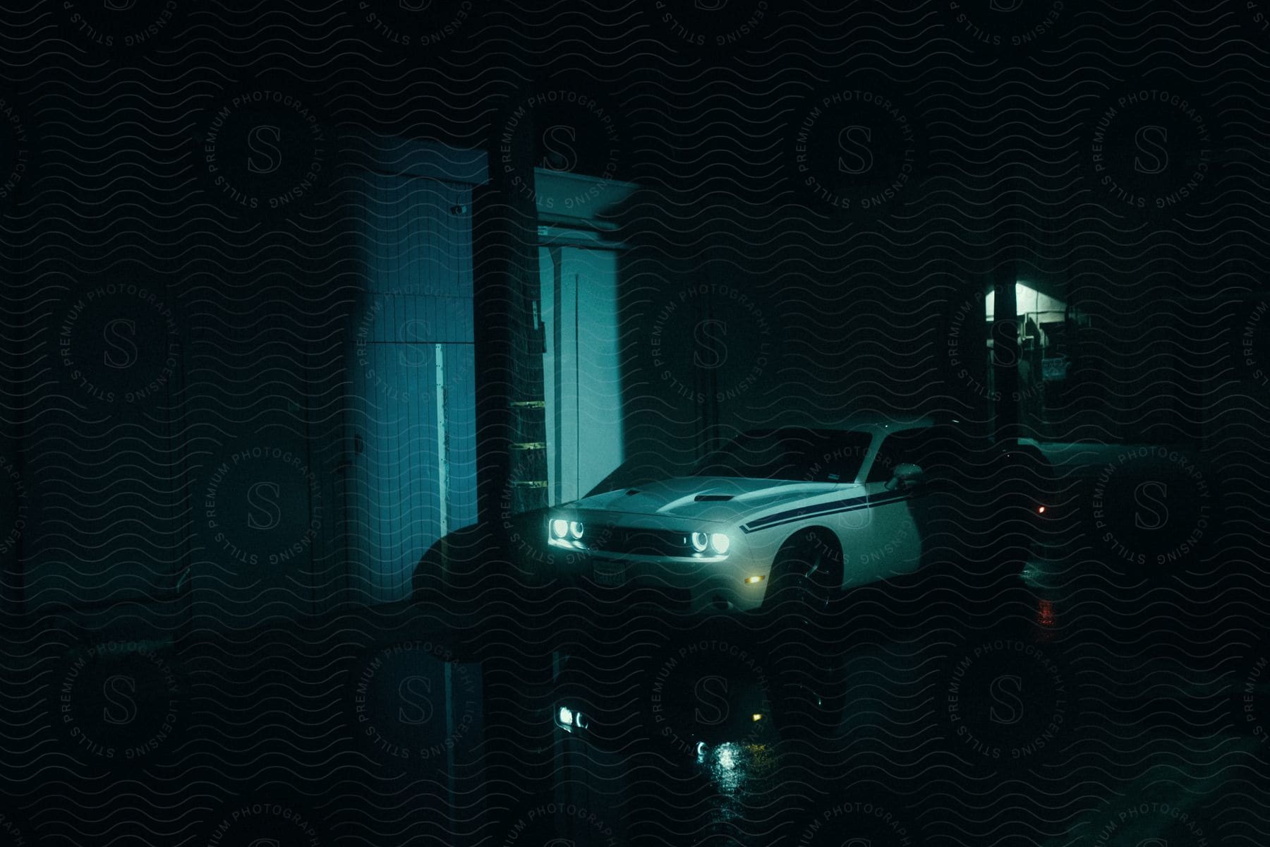 A sports car parked next to a building at night with its headlights on