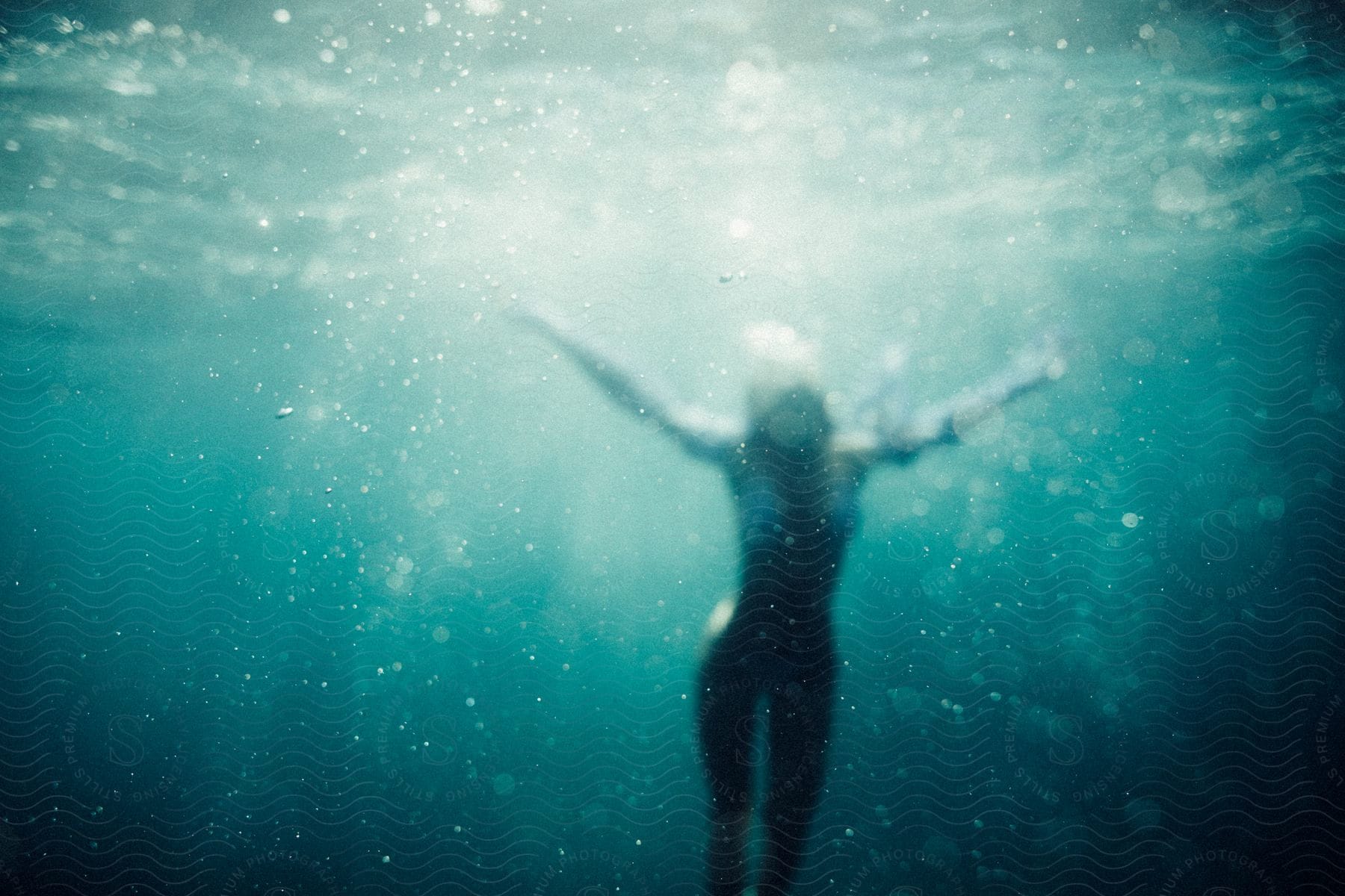 A woman swimming underwater with her arms out as she rises toward the surface