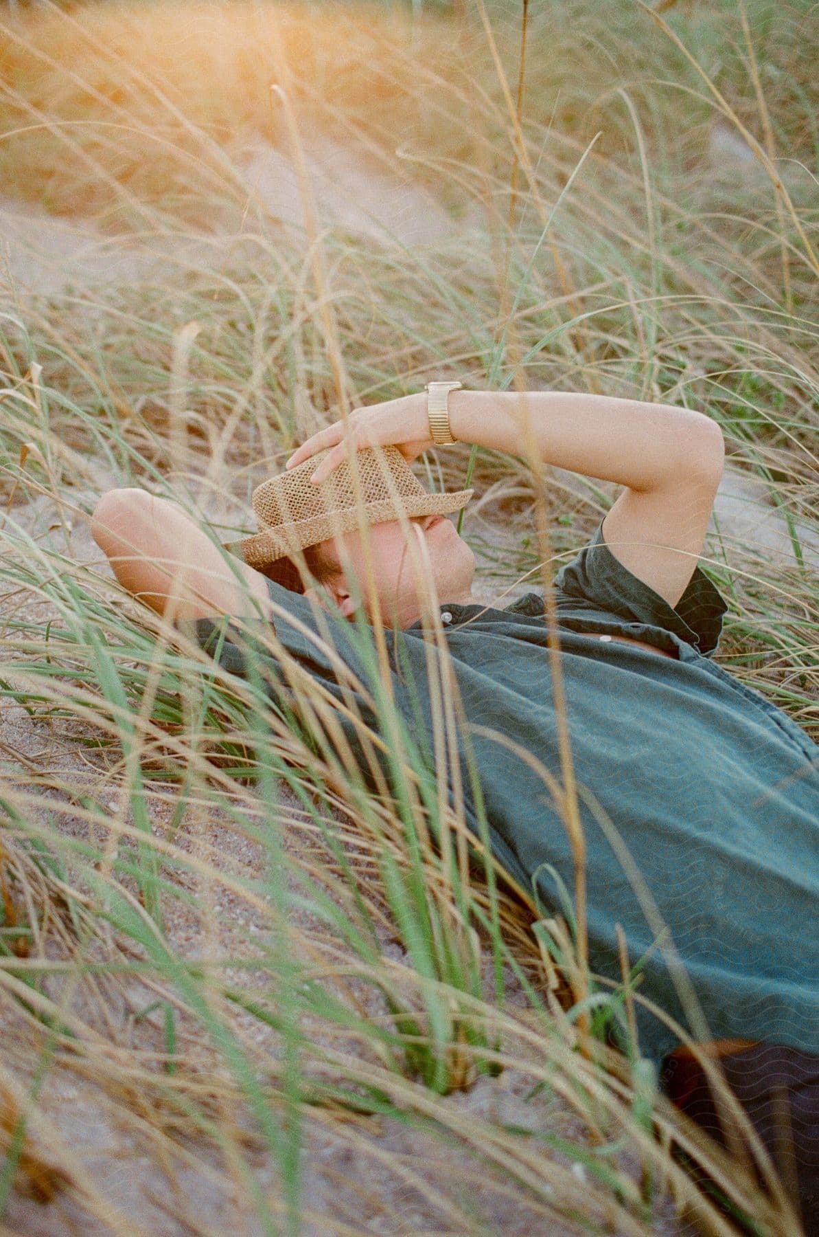 A man laying outside on grass with a hat over his head