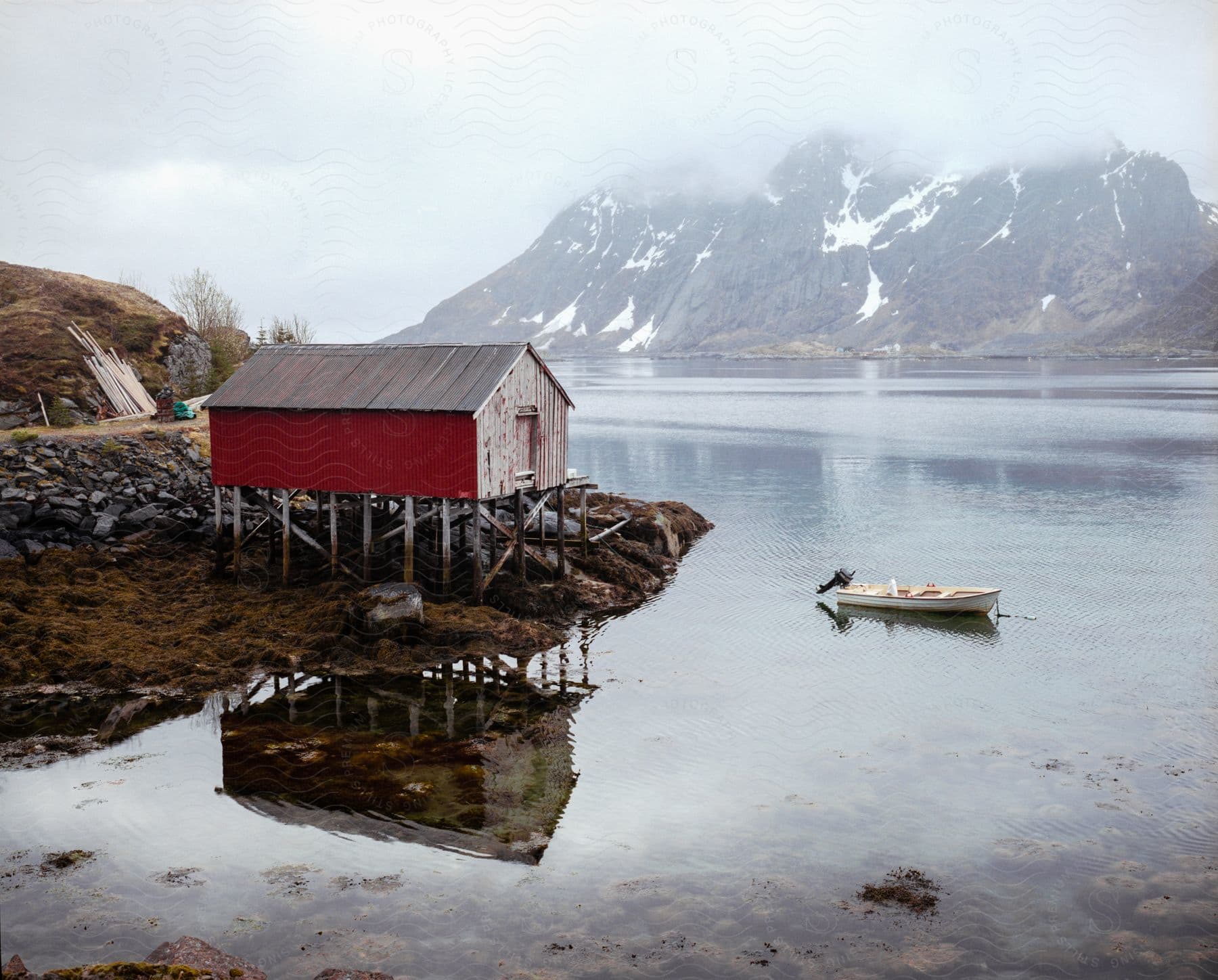 A small boat sits in the water near a shed on the coast of a mountain lake