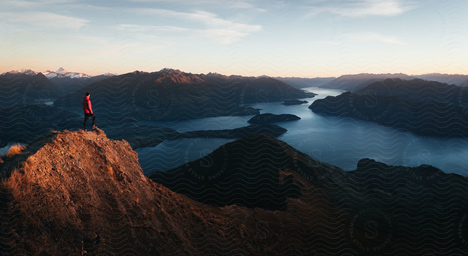 A person standing on a cliff admiring the scenic view of mountains water and sky in new zealand