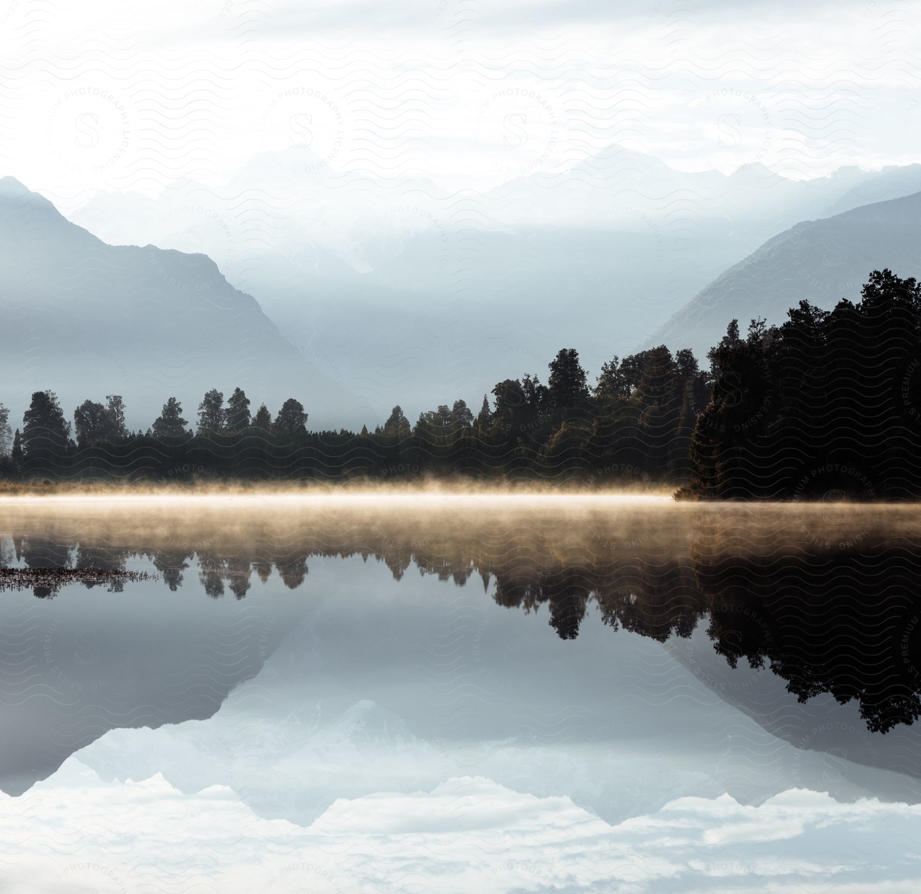 Landscape of still lake and distant mountain in fog