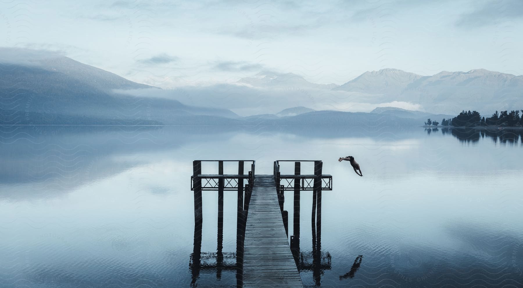 Wide natural landscape with a man jumping from the pier into the water in new zealand