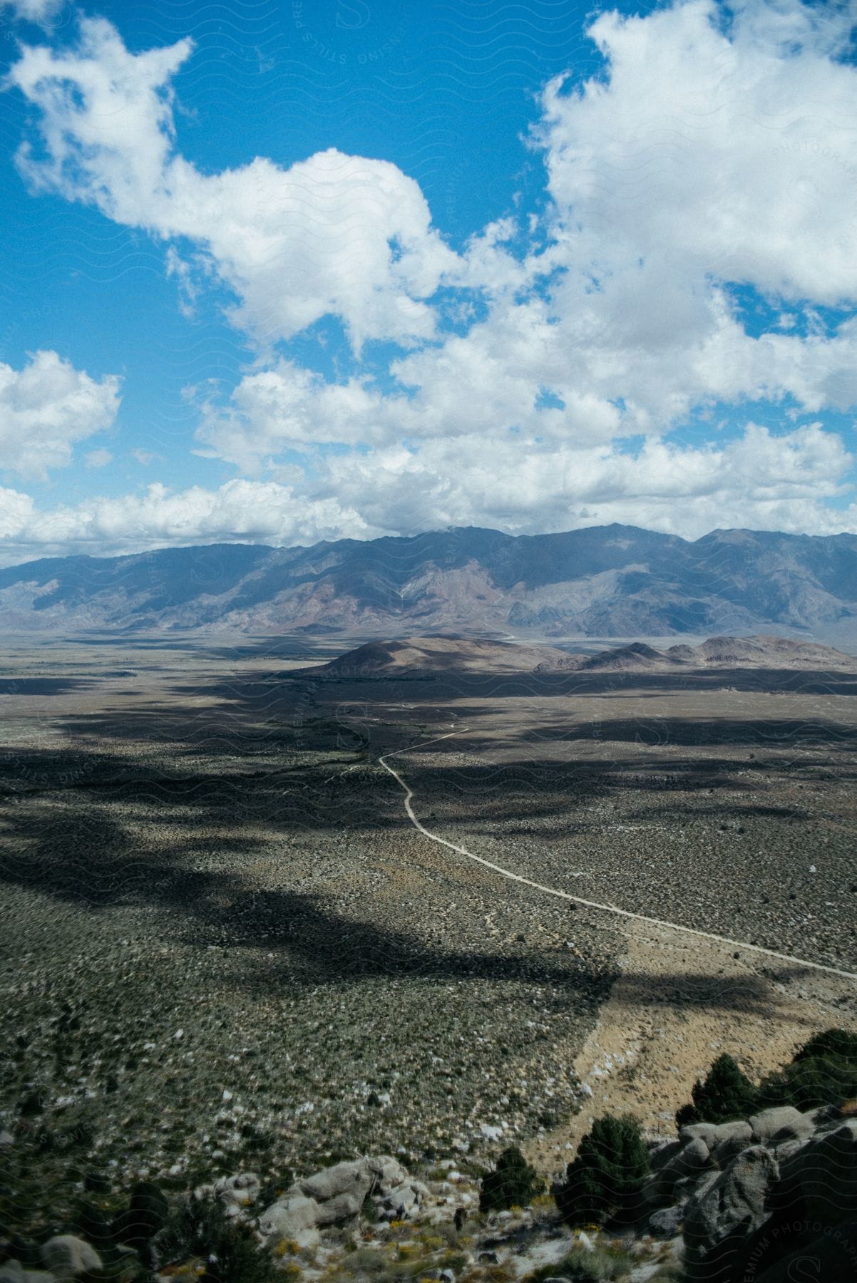 White clouds in a blue sky cast shadows on an arid brown plain and mountainous background