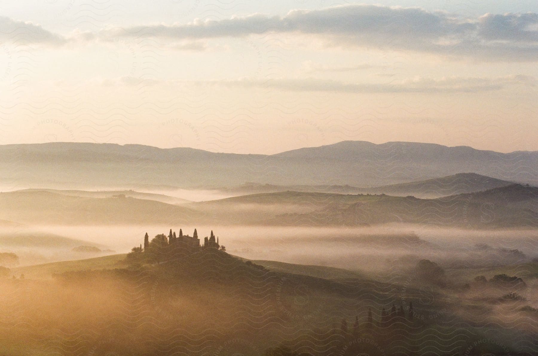 A house on a green hill with morning fog and mountains in the distance