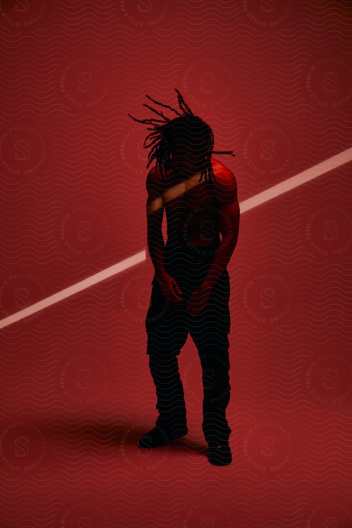A man posing in a dark room with a red wall and a beam of light on his skin