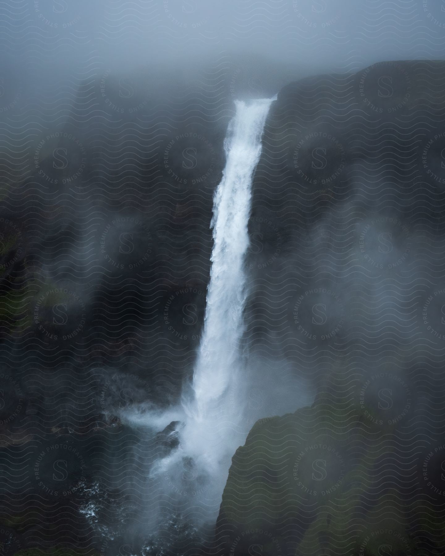 A foggy day in the mountains with a waterfall cascading from a large rock