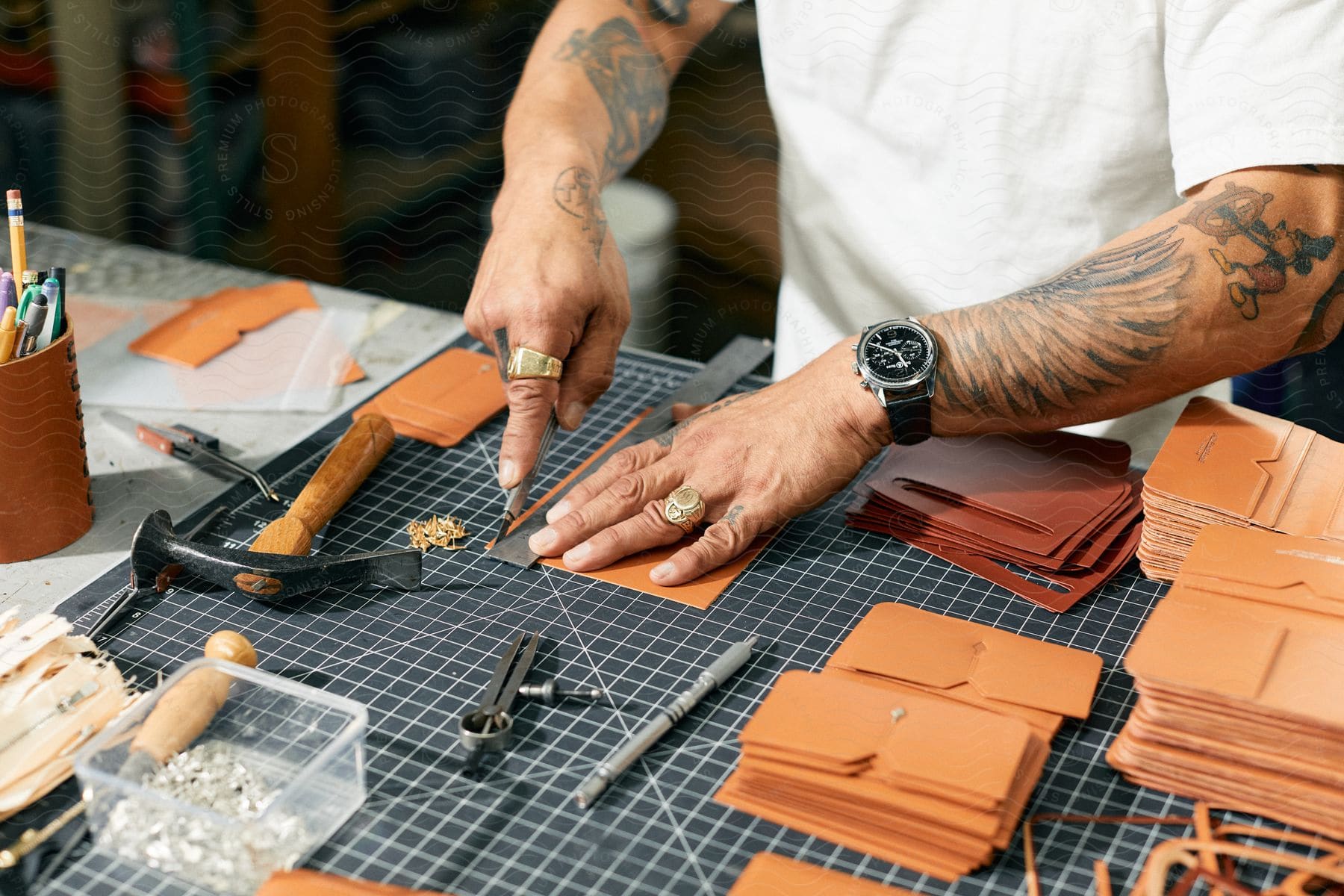 Close up of a tattooed craftsmans hands working on leather wallets over a workbench