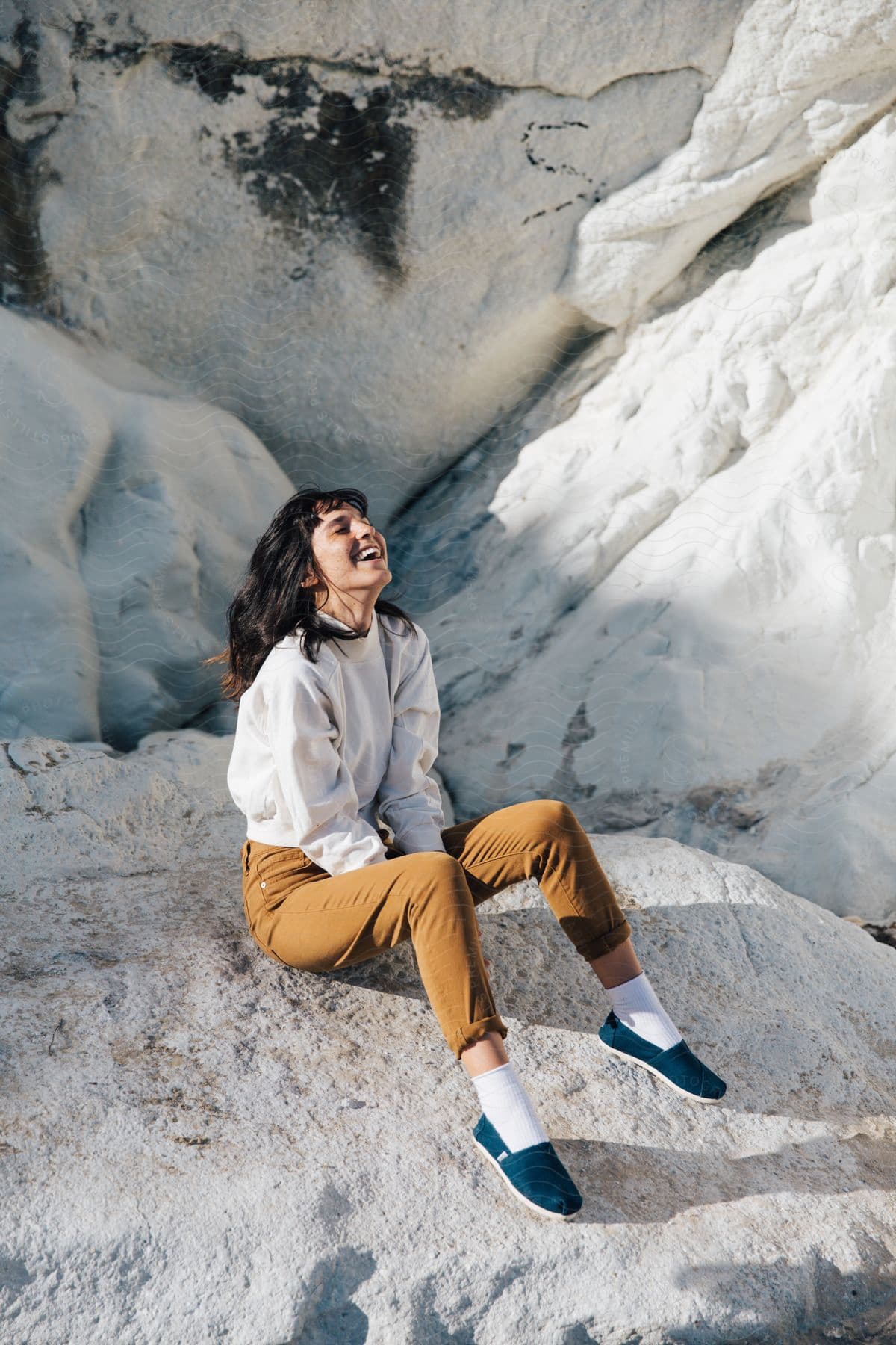 A young woman sitting on bedrock outdoors wearing sunglasses and a smile