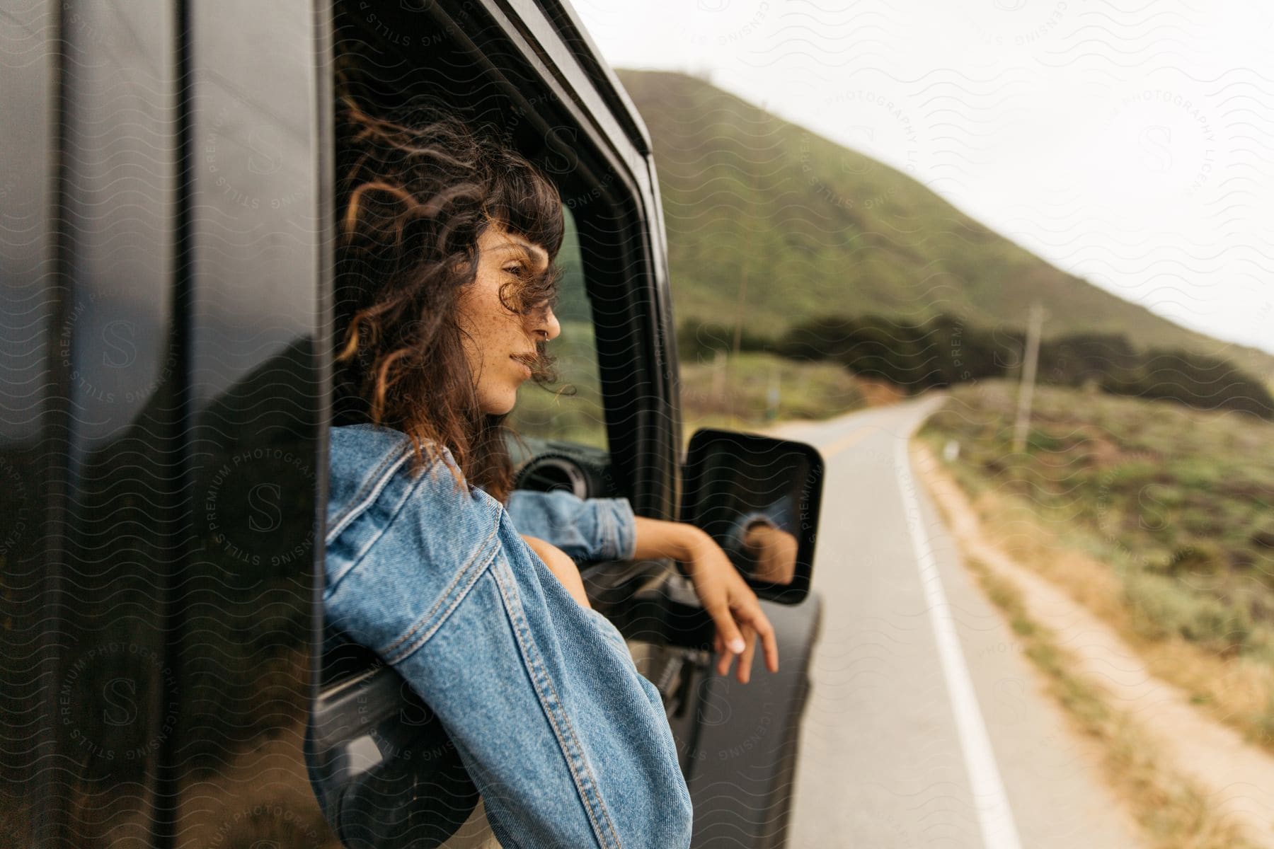 A woman leans out of the passenger window of a truck traveling near a mountain
