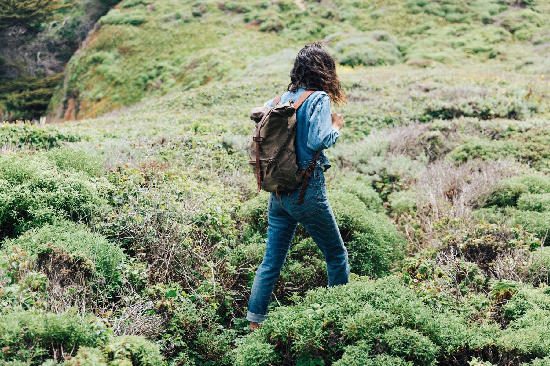 A woman hiker walks on a mountain hill while holding the strap of her backpack