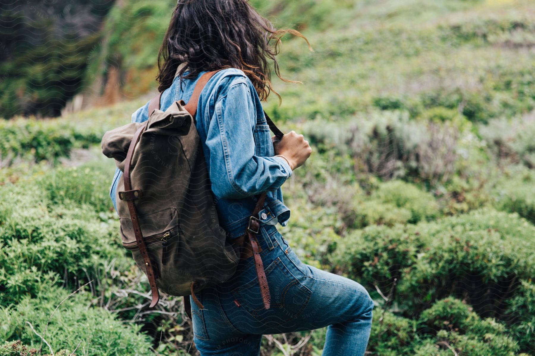 A woman walks up a mountain hill holding the strap of her backpack