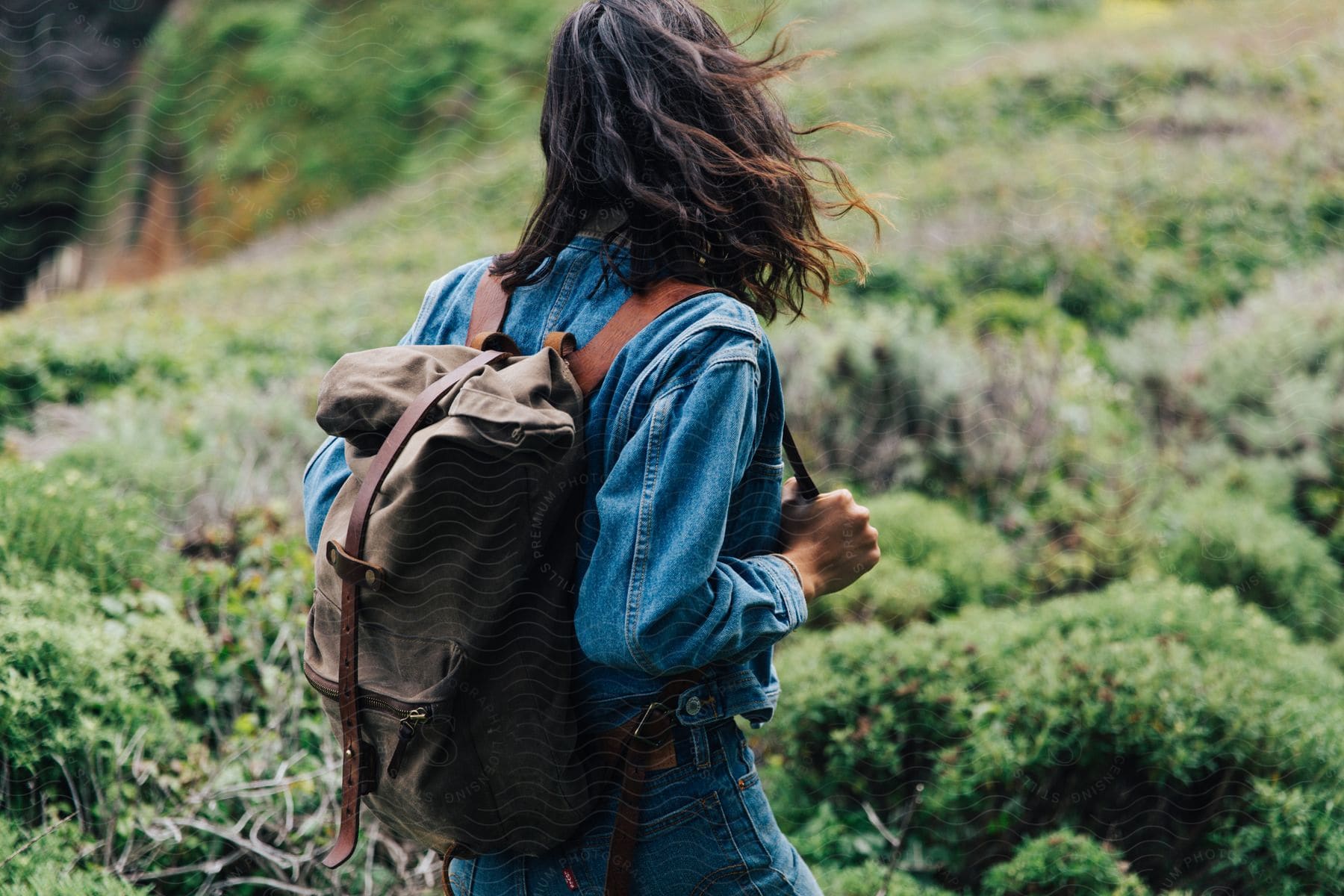 A woman walks up a mountain hill holding the strap of her backpack