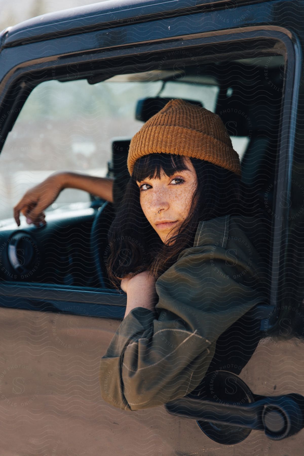 A woman sits in the drivers seat of a truck her arm resting on the door as she looks out the open side window