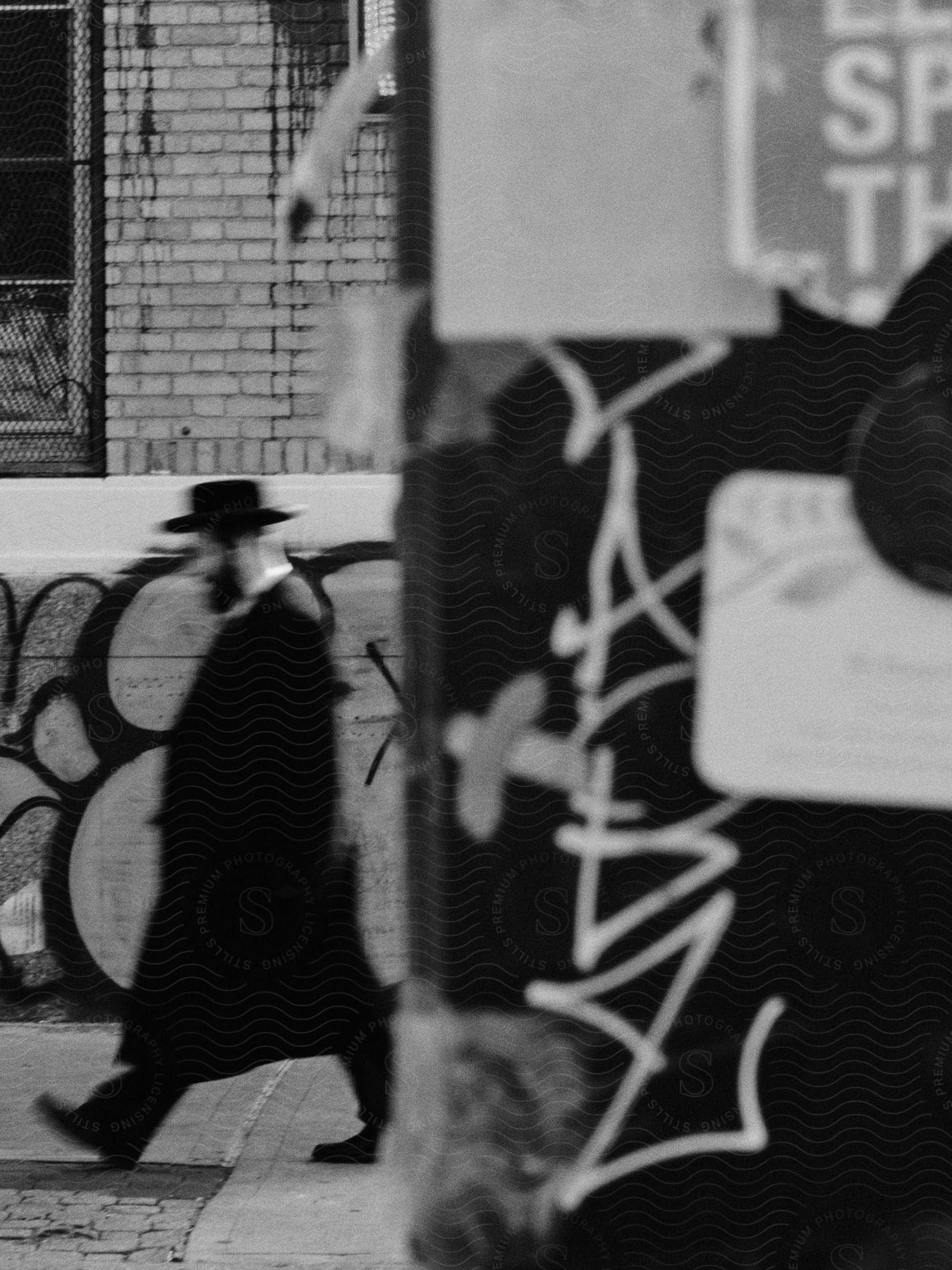 A man wearing a hat beard black overcoat and shoes walks down a street in new york city