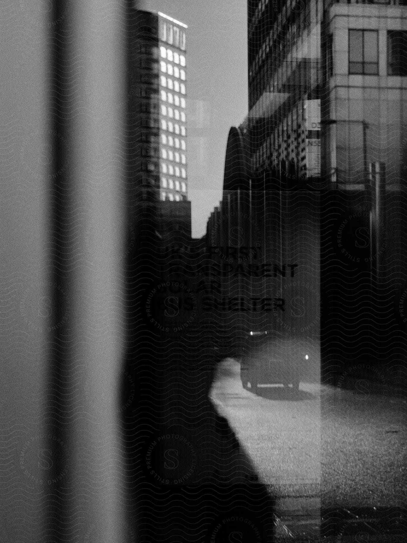 Black and white shot of a car on a city street reflected on a window in daytime