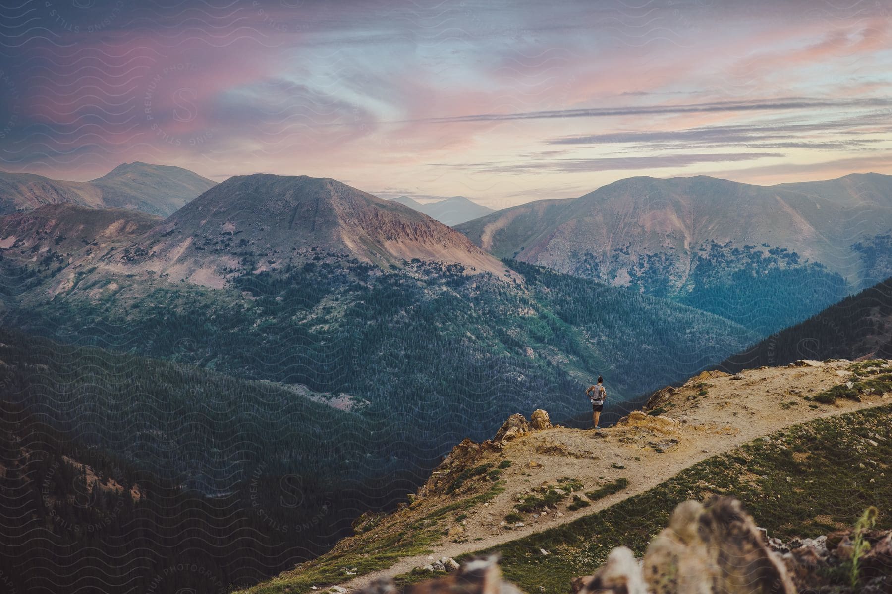 Distant hiker watches high mountain range at sunset