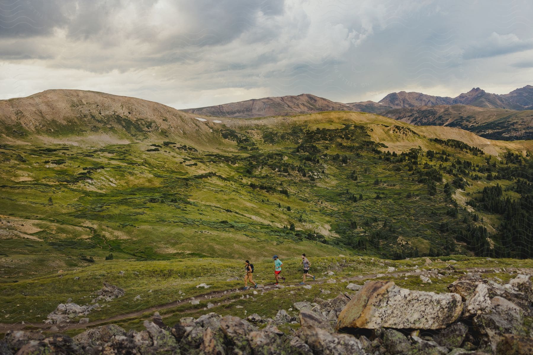 Three people running on a mountain path on a cloudy day