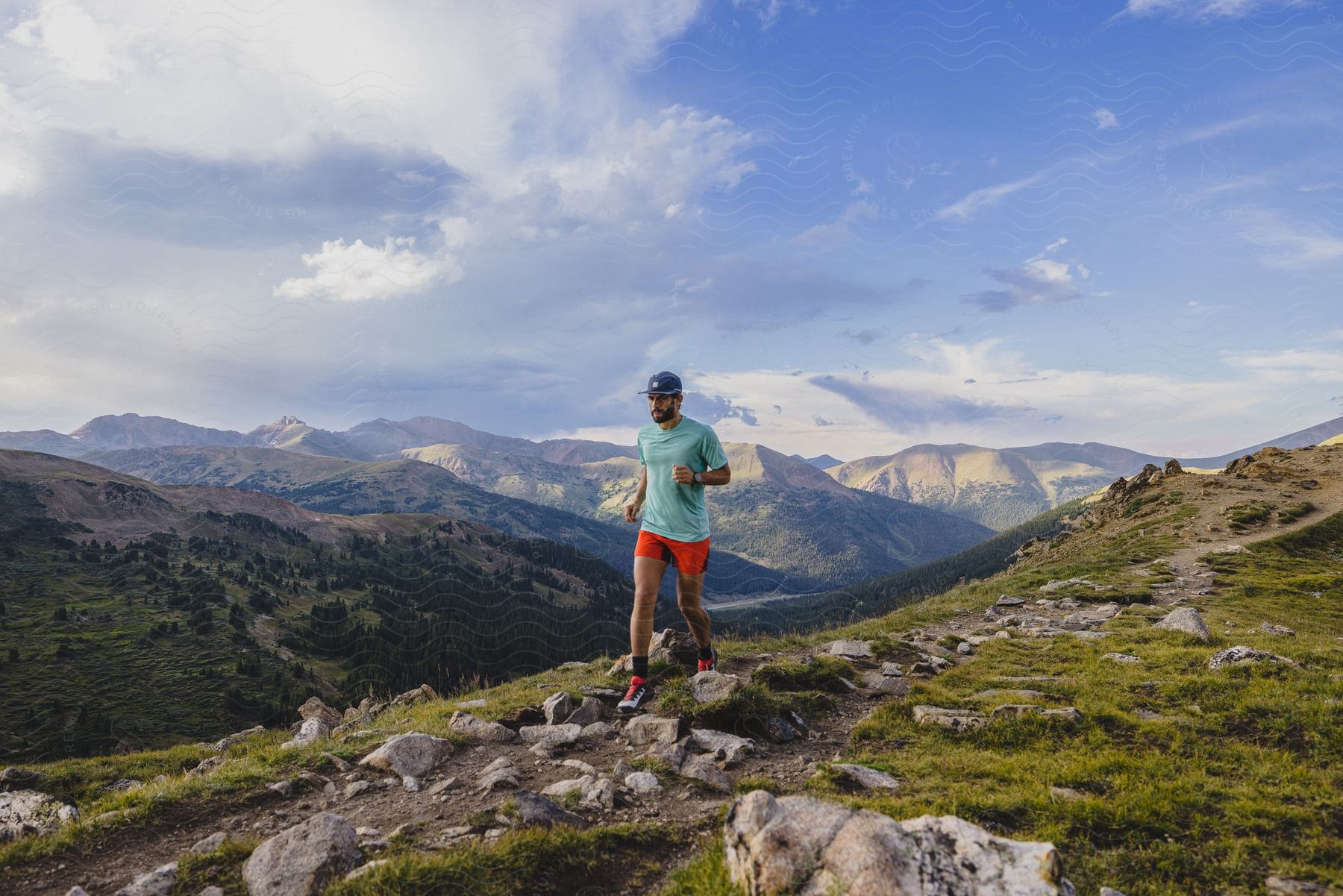 A man jogging on a rocky trail with mountains in the distance under a cloudy sky