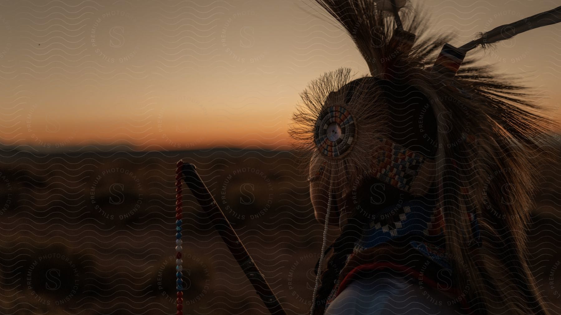 A native american teenager wearing a headdress stands outside at dusk