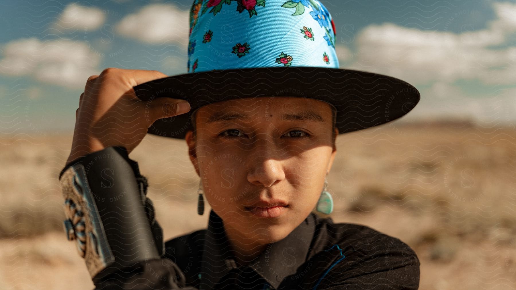 Woman wearing a colorful hat stands on the desert looking at the camera