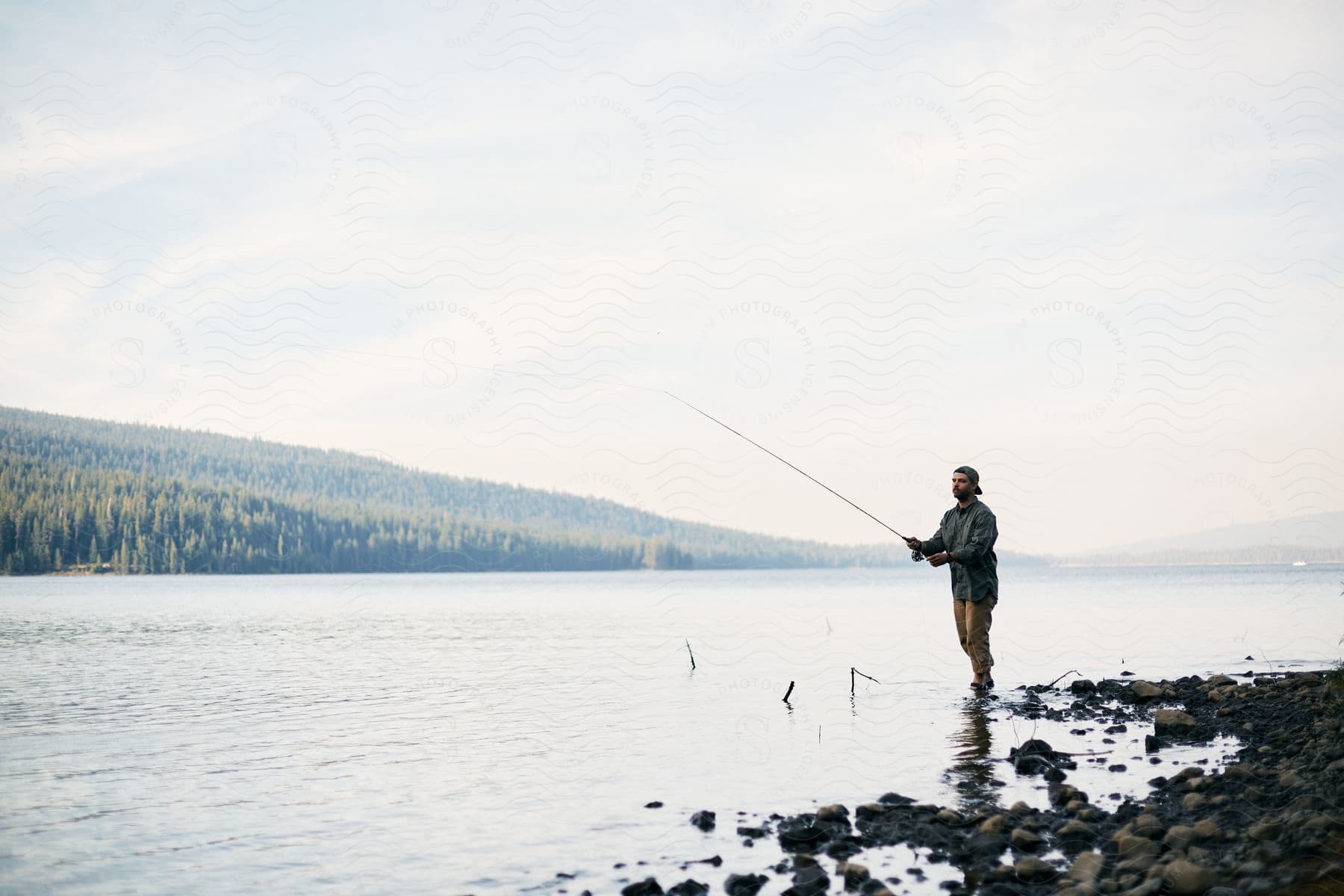 A single person fishing by a lake with a bird flying overhead