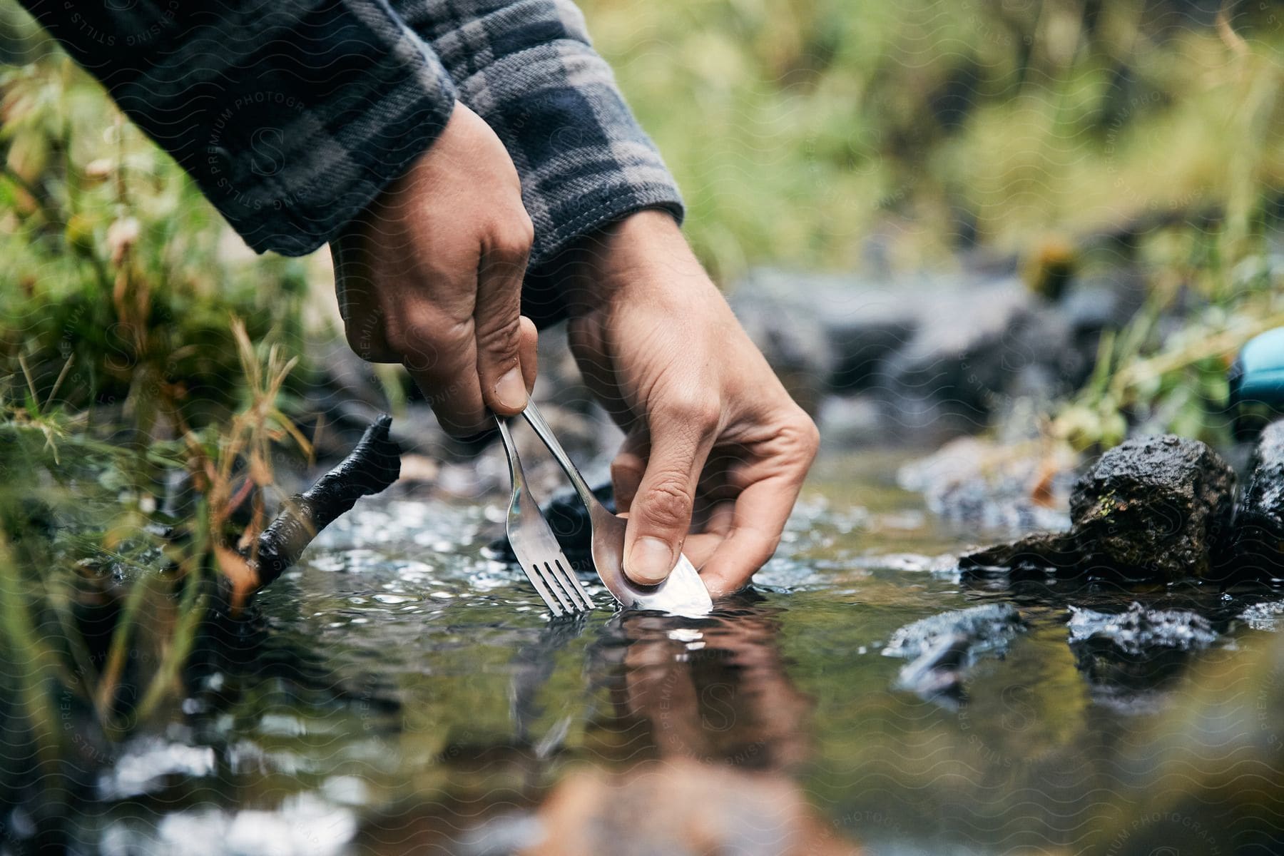 A person washing silverware in a stream