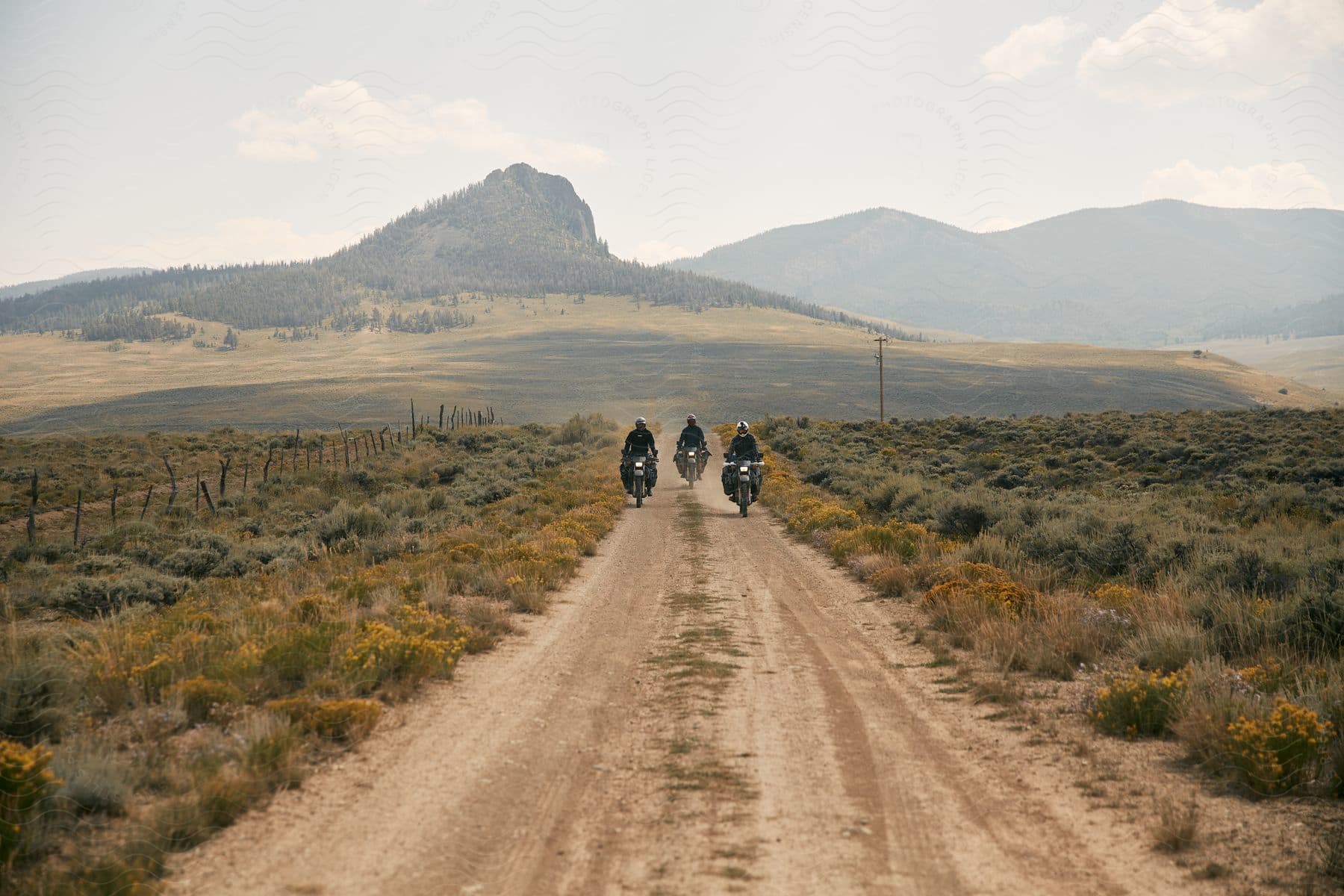 Three people riding a motorcycle through a mountainous landscape under an open sky