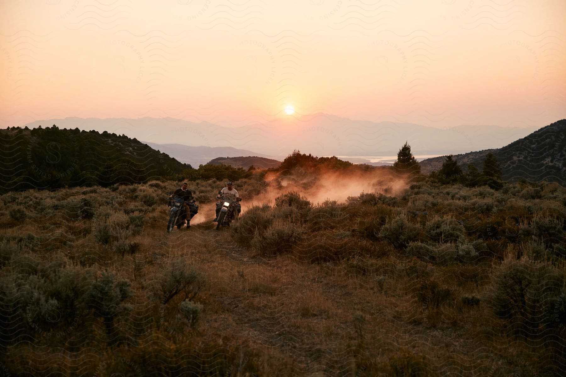 Two people riding a motorcycle through a mountainous landscape at dusk