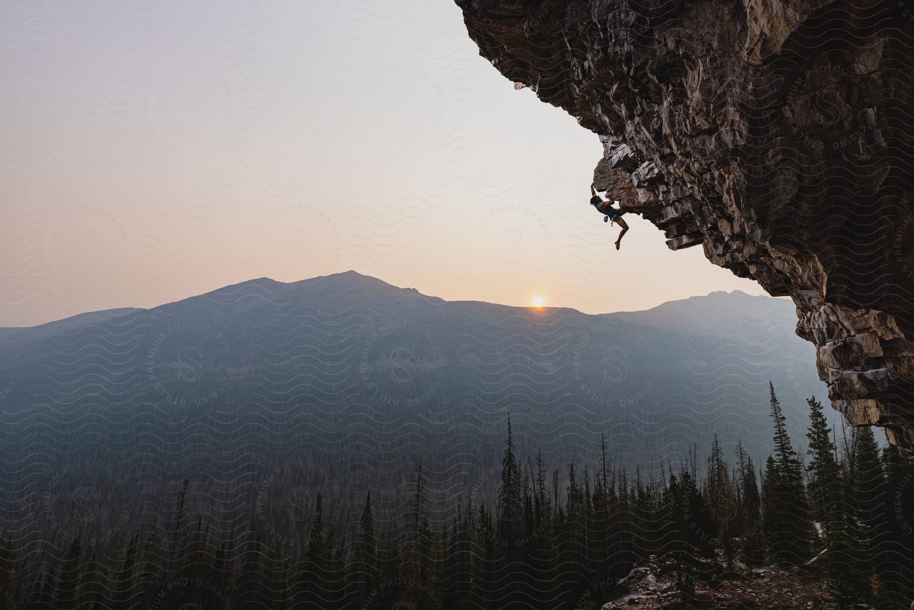 Climber scales cliff with mountains in background at sunset