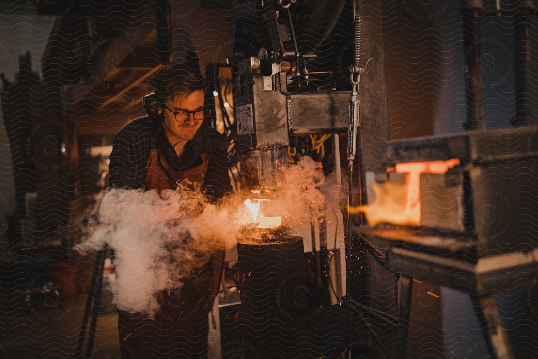 A determined adult male working with hot metal and machinery in a studio to create a forged item