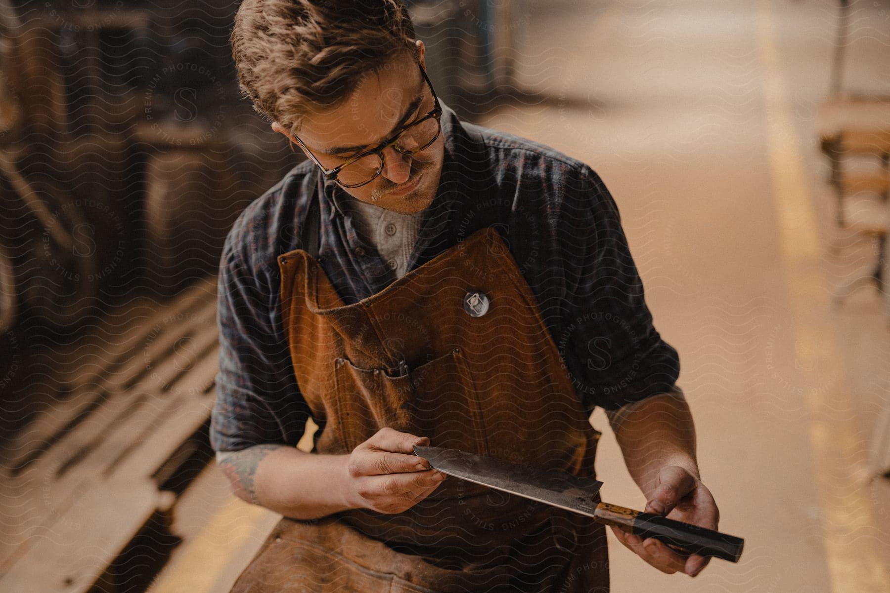 Young craftsman wearing a leather apron inspects a knife in a warehouse