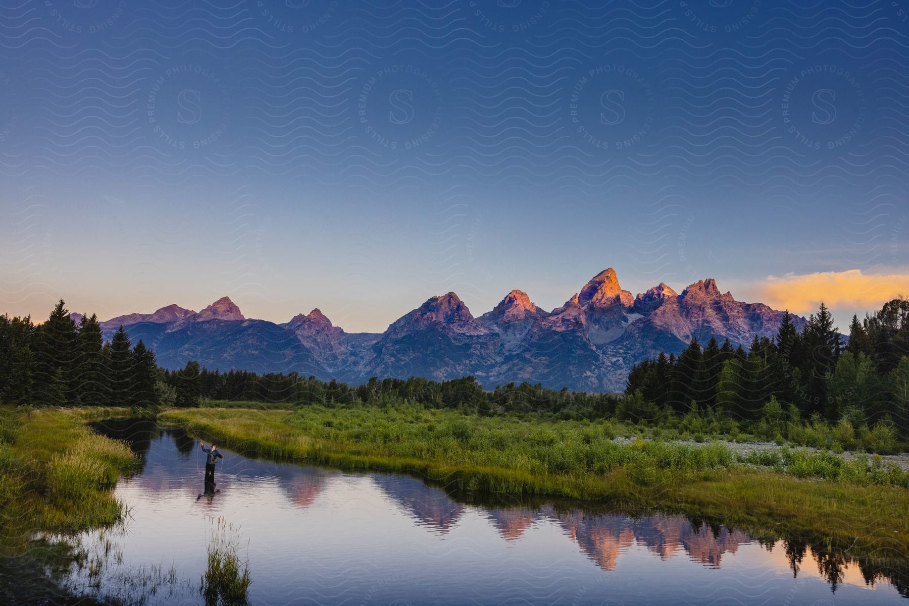 A sunset landscape shot of a river in front of a forest and mountain range