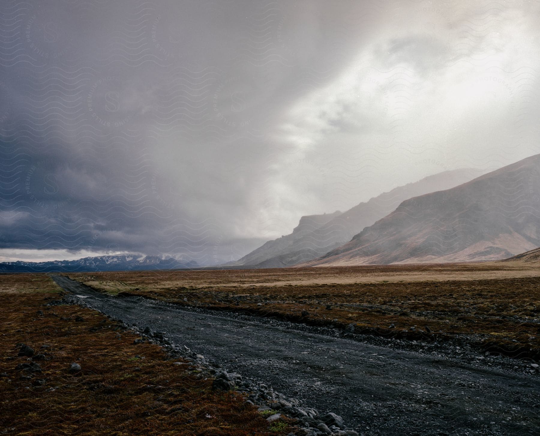 A road winds through a mountainous landscape with clouds overhead