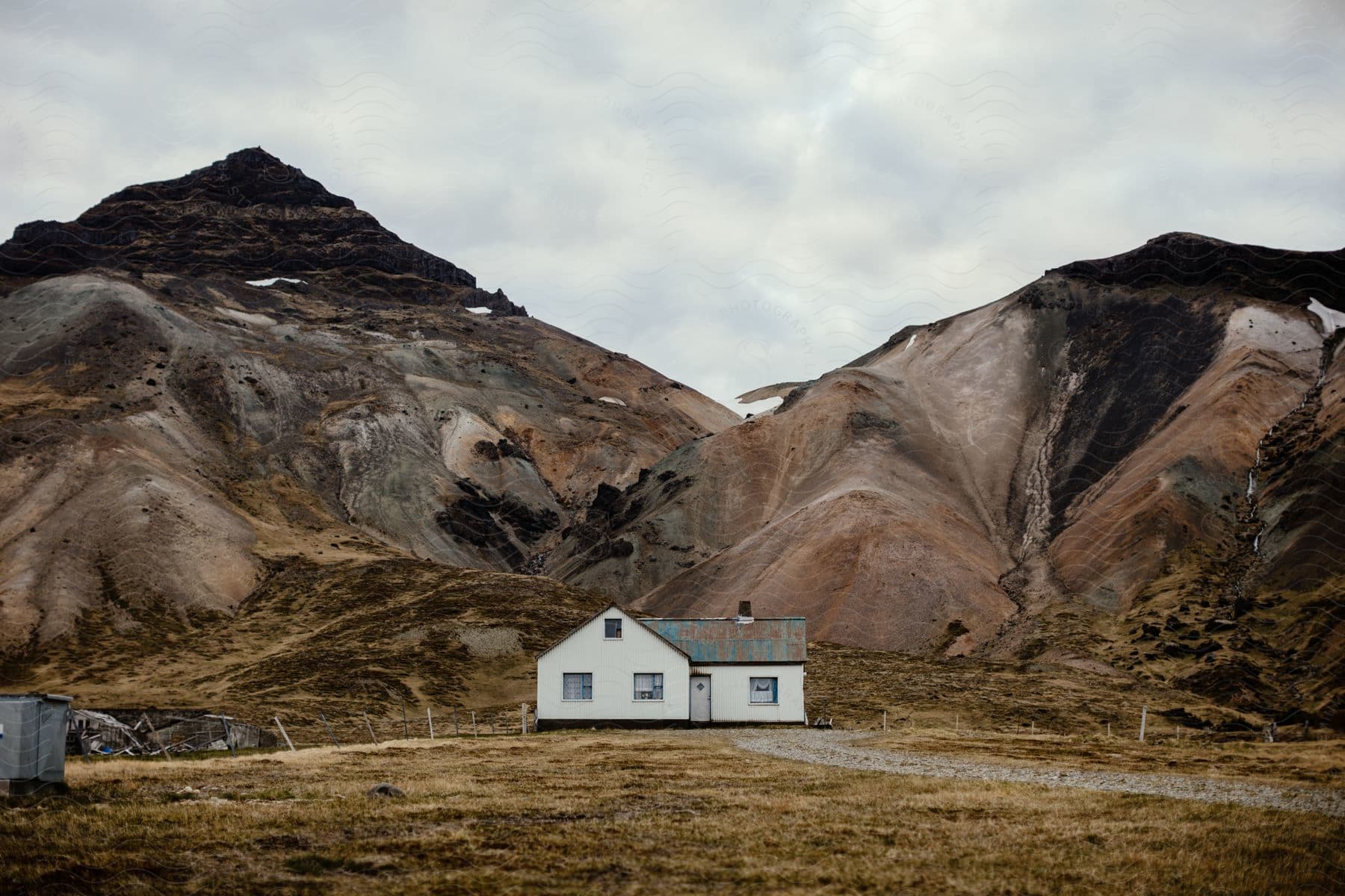 A white house sits at the foot of two mountains under a cloudy sky in iceland