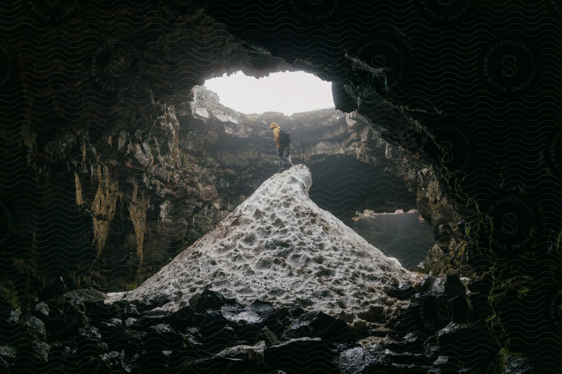 A hiker climbs on top of a melted snow mound in a cave on a sunny day in iceland