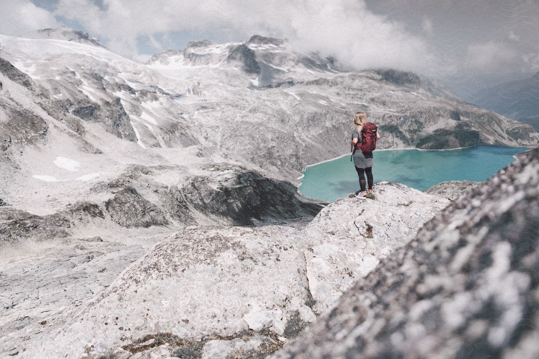 Stock photo of a female hiker stands on rocks overlooking a lake in the alps