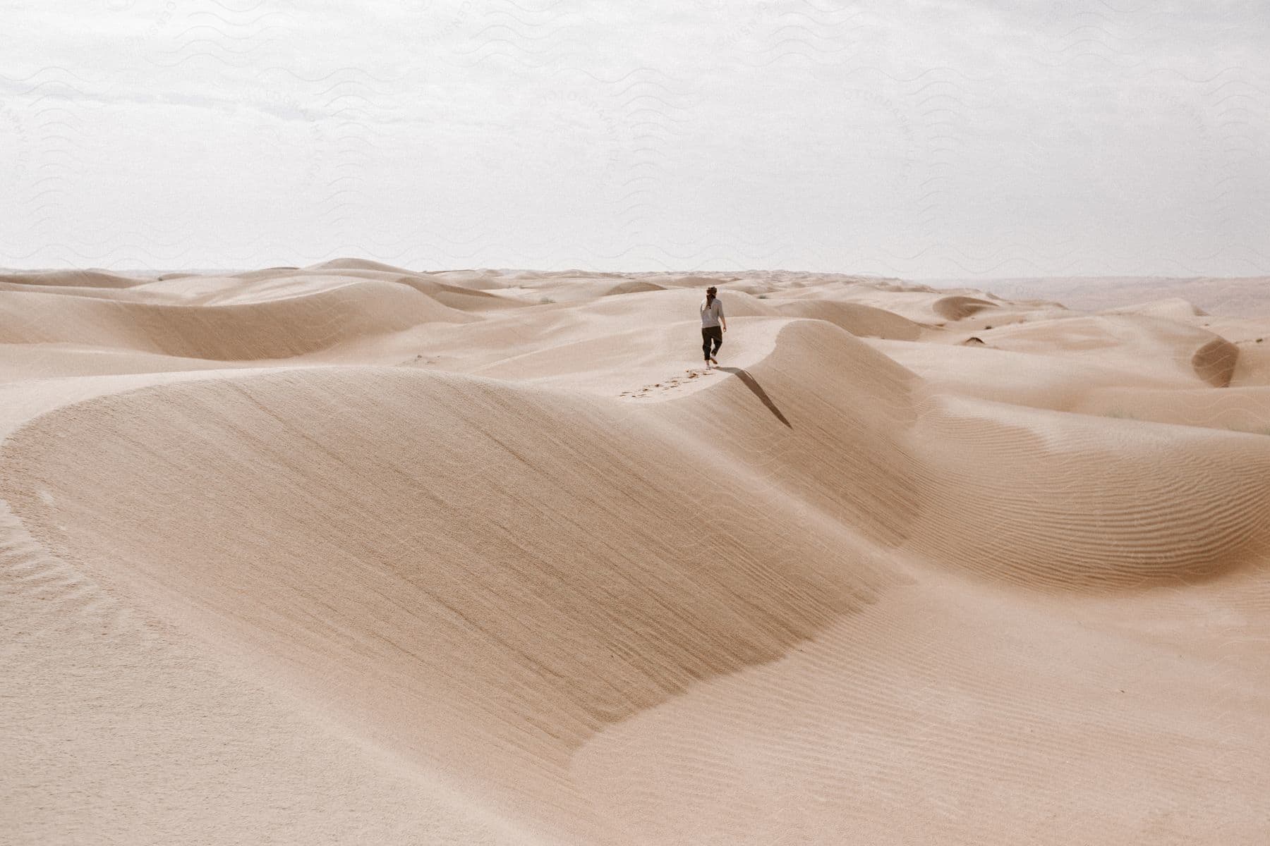 Distant man walks along sand dune in the desert