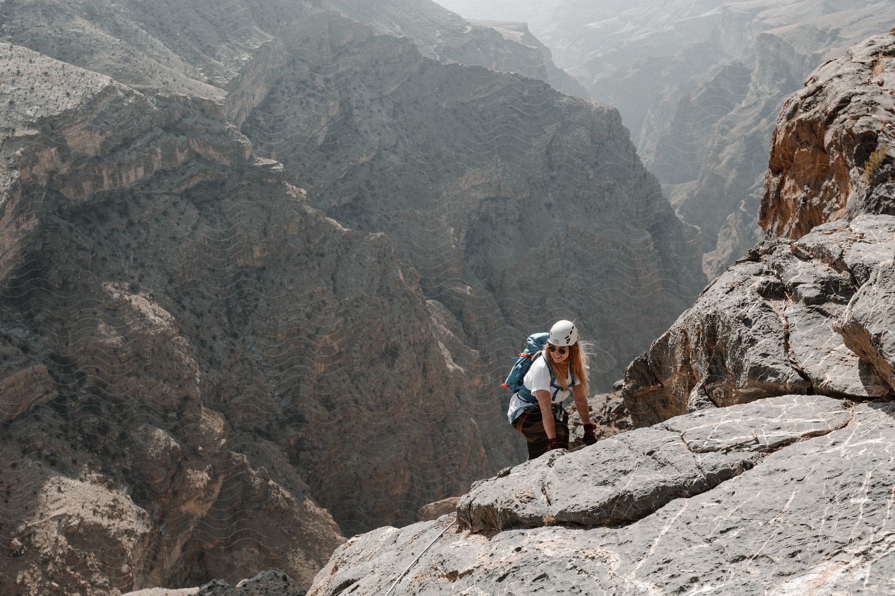 A woman climbing a mountain during spring with a backpack and helmet