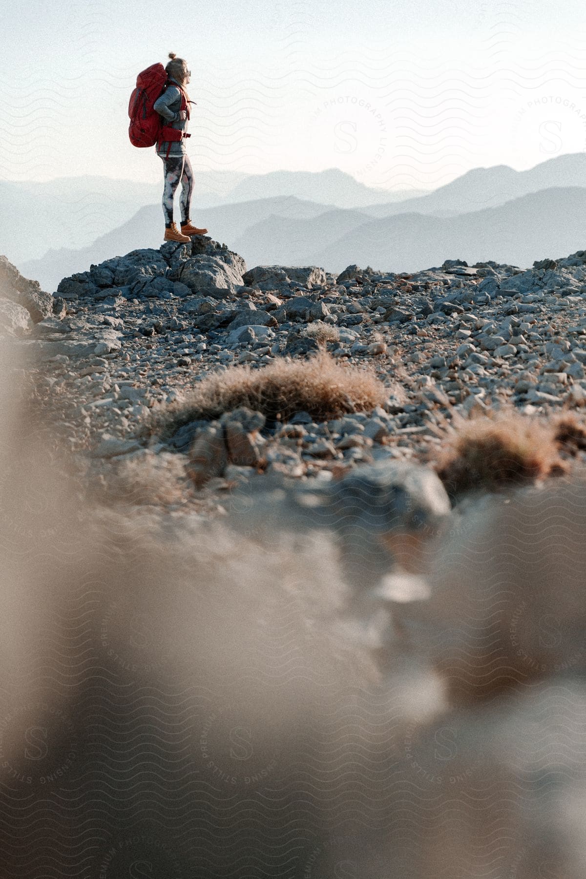 Blonde woman hiking at the peak of a mountain with other mountains in the distance