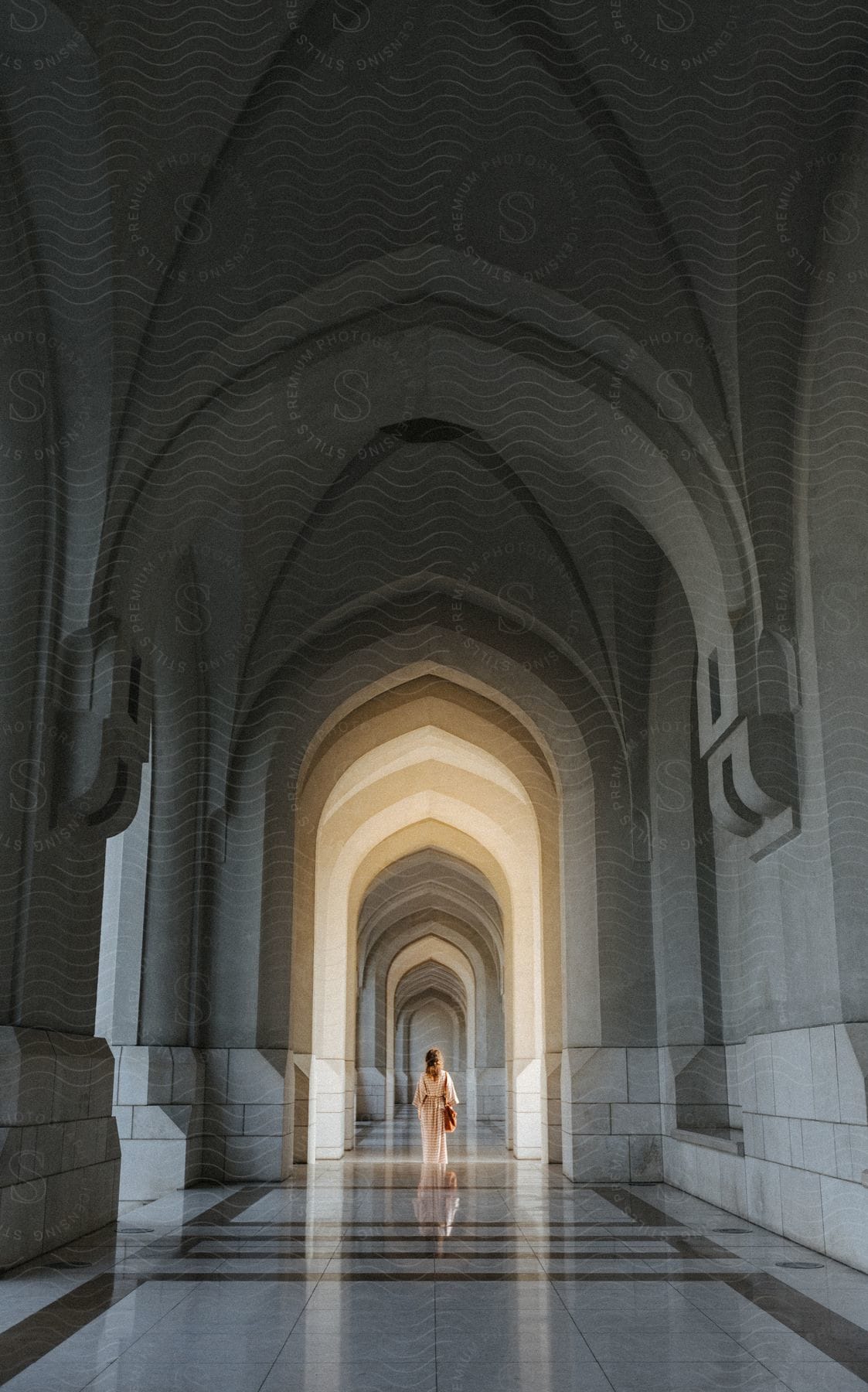 A woman walks down a hallway with tall gothic archways and a polished marble floor