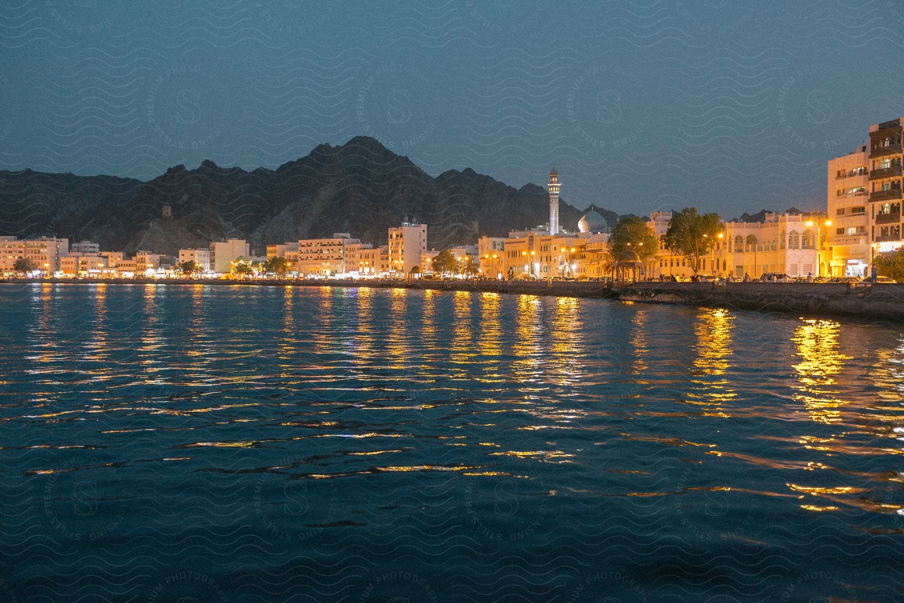 A city lines the shore of a lake with mountains in the background