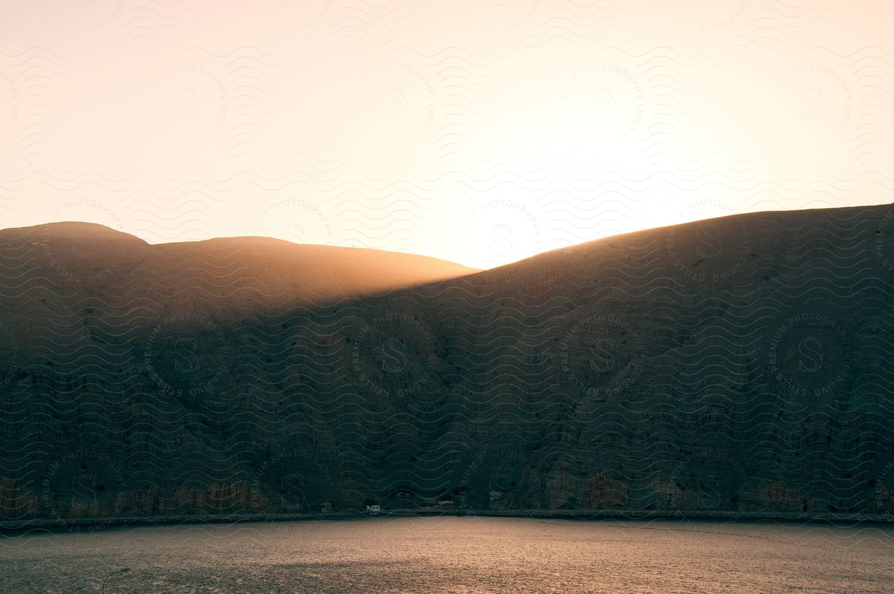 Sunlight bursts through a dip in a hillside next to a body of water