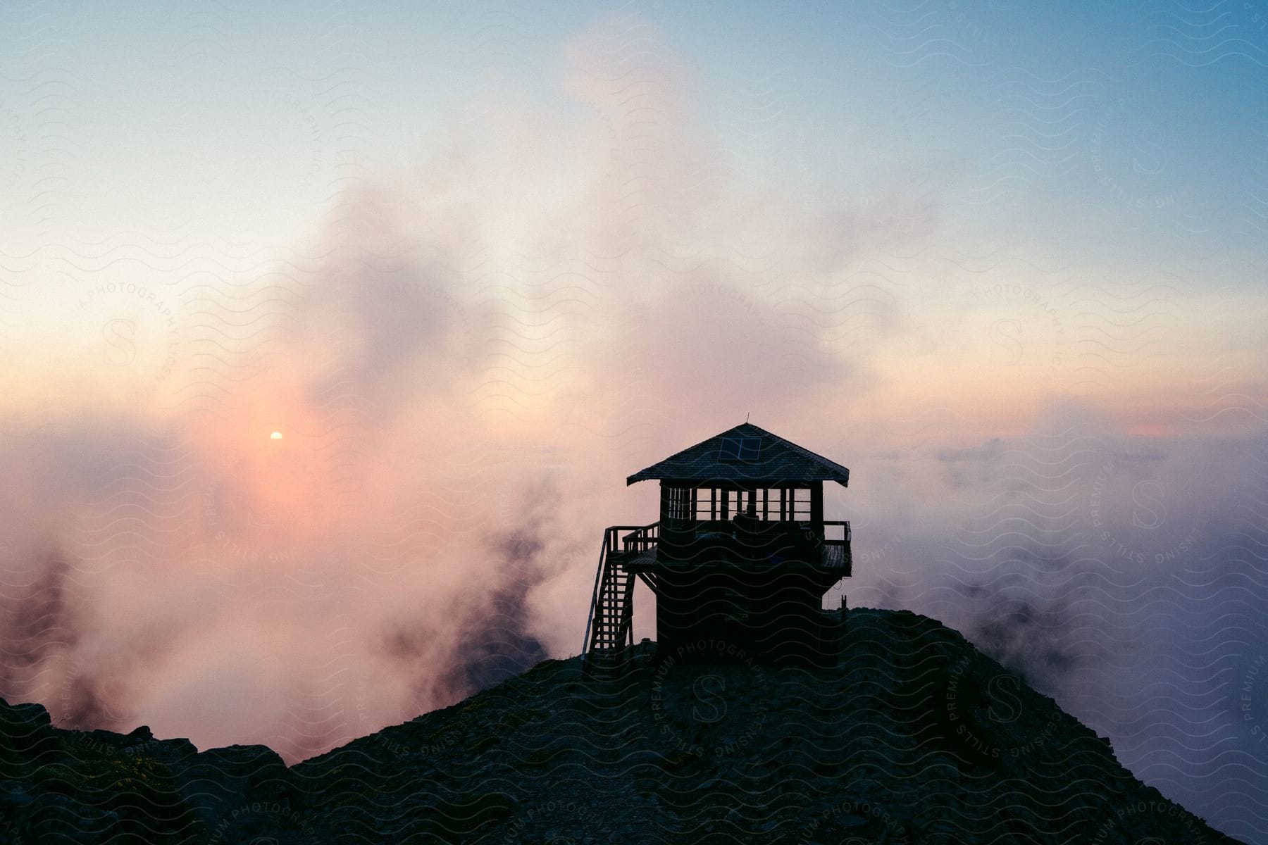 A silhouette of a mountaintop structure with fog rising from the valley as the sun rises
