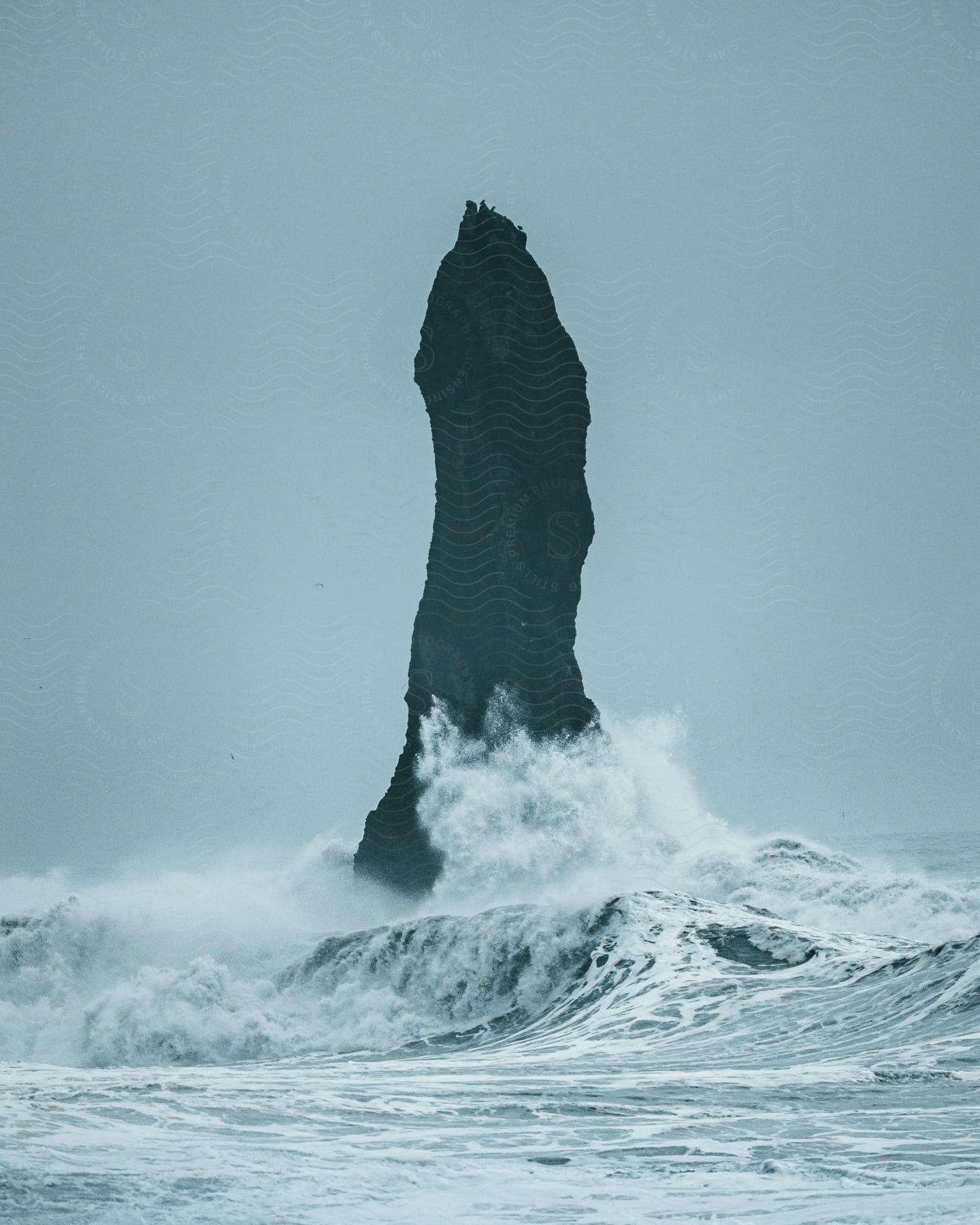 A tall rock in the middle of the sea with a clear sky