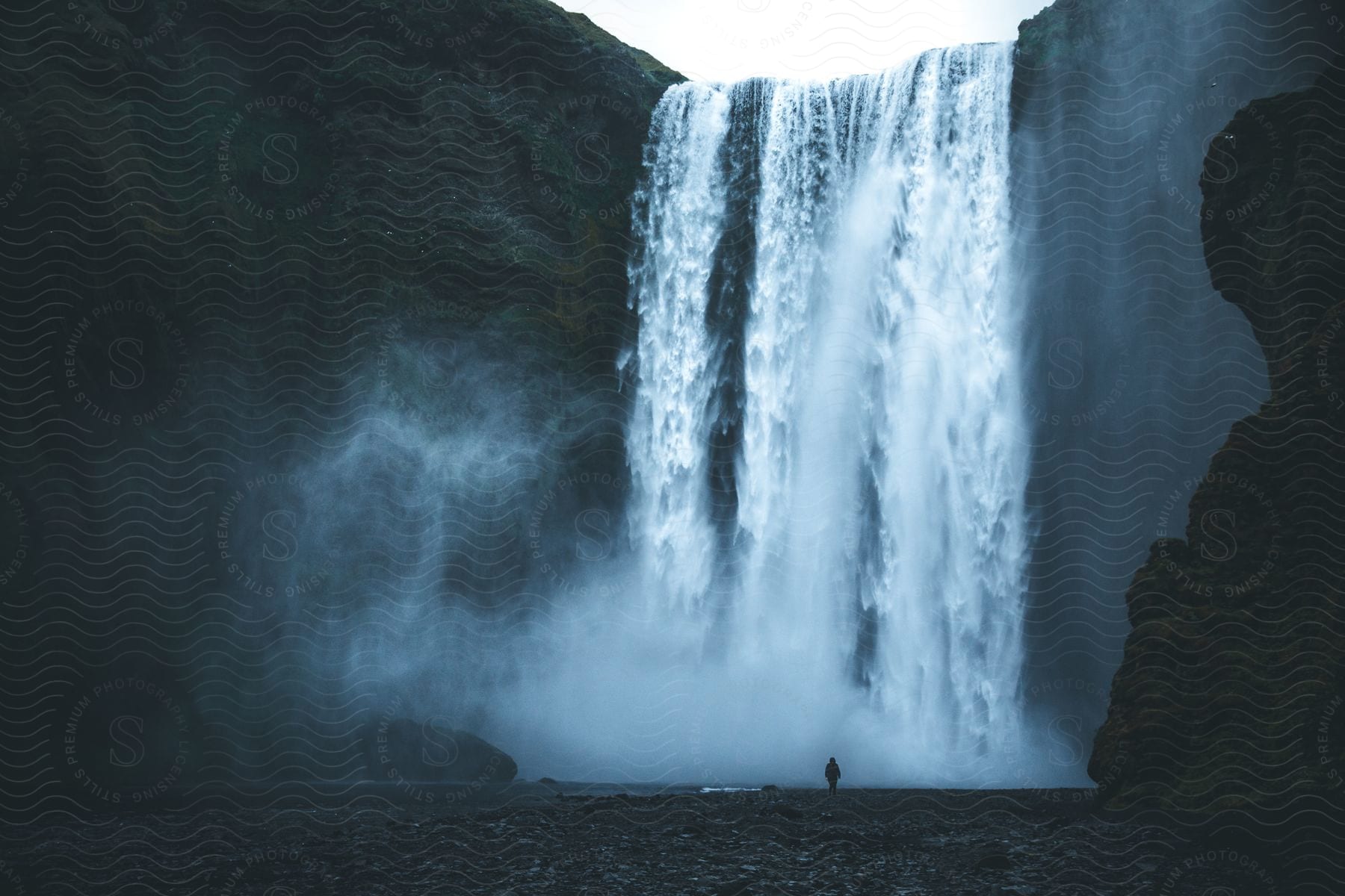 A person is walking near a waterfall at midday in iceland