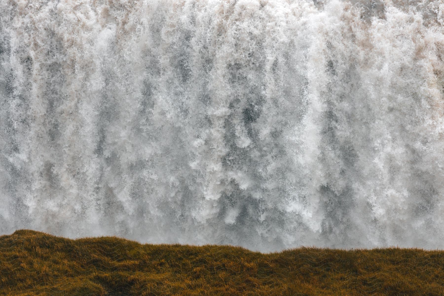 A large waterfall with bubbles and a land with some grasses in iceland