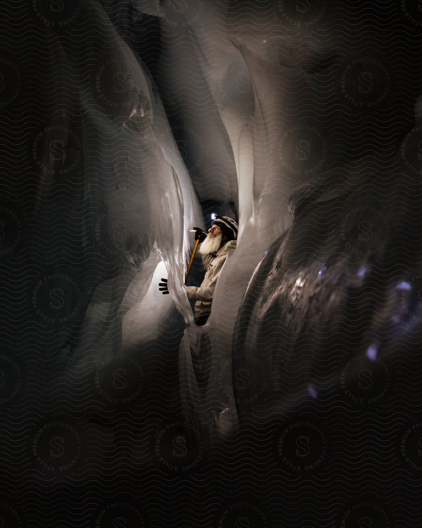 Bearded male ice climber with an ice axe in his right hand wearing a headlamp inside an ice cave